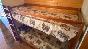Kerrossänky kuviollisilla vuodevaatteilla huoneessa, jossa on puuseinät ja ovi.