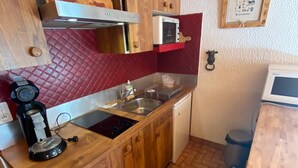 Kompakti keittiö, jossa on puukehikoiset kaapit, sisäänrakennettu mikroaaltouuni, pesuallas ja pienikokoinen liesi.