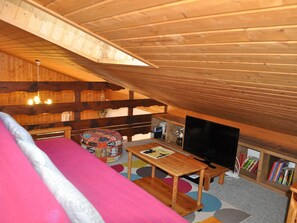 Um quarto de sótão aconchegante com teto de madeira, uma cama, uma TV e uma estante.