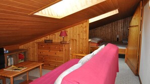 Ett mysigt sovrum på vinden med ett träpanelat tak, en våningssäng, en byrå och ett litet bord med en lampa.