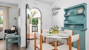 A dining area with a round table, white chairs, and a teal cabinet with shelves. - UDANE (Cala´n Blanes)