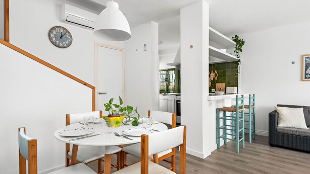 A modern kitchen with white cabinets, a dining area with a round table and chairs, and a staircase leading to another level. - UDANE (Cala´n Blanes)