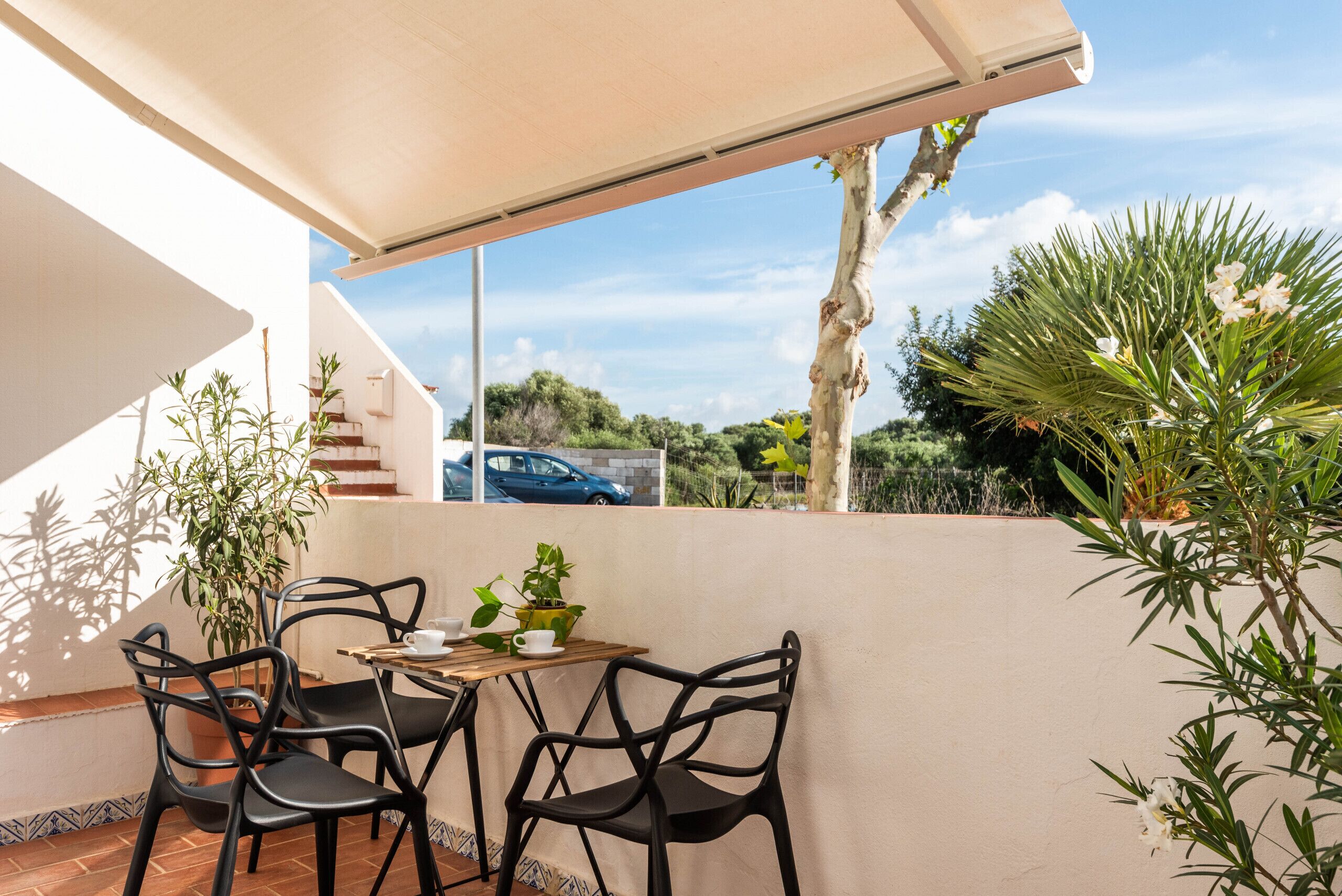 A patio with a table and chairs, surrounded by plants and a view of the street.