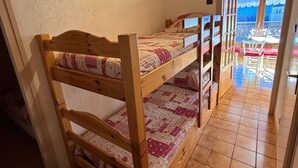 Un lit superposé avec une tête de lit et un pied de lit en bois, une couvre-lit à motifs et une petite commode en bois.