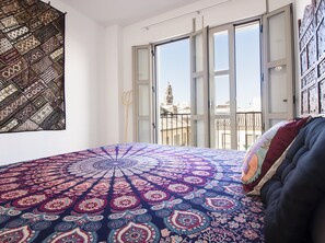 A bedroom with a large bed, a view of the city through a sliding glass door, and a tapestry on the wall.
