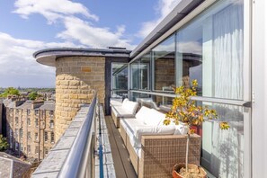 A balcony with wicker furniture and a potted plant, overlooking a cityscape. - Beautiful Penthouse with Terrace & Jacuzzi (Edinburgh)