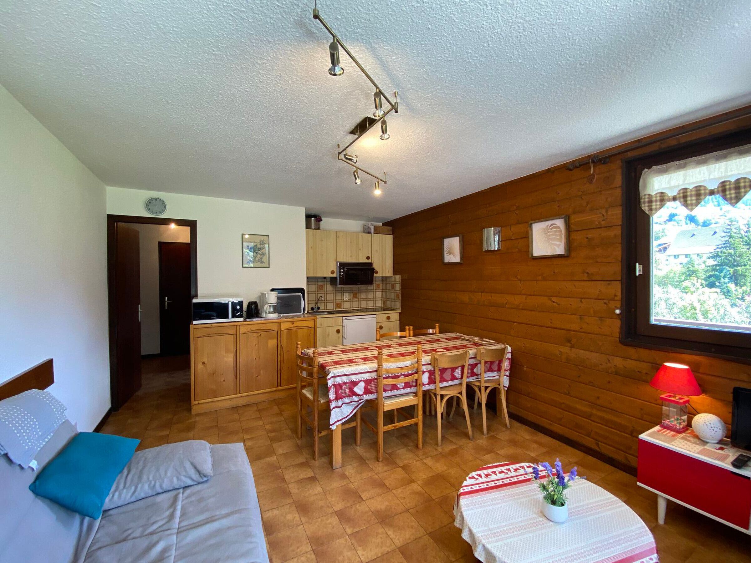 A cozy room with a bed, a dining table with chairs, a small kitchen area, and a window with a view.