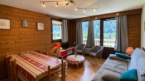 Ein gemütlicher Raum mit Holzvertäfelung, einem Esstisch mit Stühlen, einer Couch und einem Fernseher auf einem Schrank.