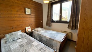 Ein Zimmer mit zwei Betten, Holzwänden, einem Fenster mit Vorhängen und einer hängenden Leuchte.