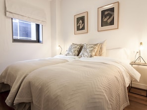 Ein Schlafzimmer mit zwei Betten, einem Fenster mit Jalousie und zwei gerahmten Bildern an der Wand.