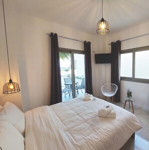 Quarto de hotel com uma cama grande, duas luminárias pendentes, uma televisão e vista para o exterior.