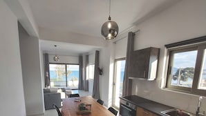 A modern kitchen with a dining area, large windows, and a view of the sea. - Finikas Suites & Apartments Airport (Spata-Artemida)