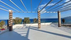 A covered outdoor area with a view of the sea, featuring a pergola structure and a white floor. - Finikas Suites & Apartments Airport (Spata-Artemida)
