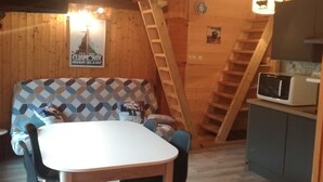 Ein gemütliches Blockhaus-Interieur mit Esstisch, Stühlen, einer Couch, einer Leiter und einer Mikrowelle.