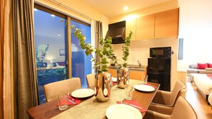 A dining area with a table set for four, a microwave, and a refrigerator in the background. - PrimeRoomBeppu Hamawakionsenmae (Beppu)