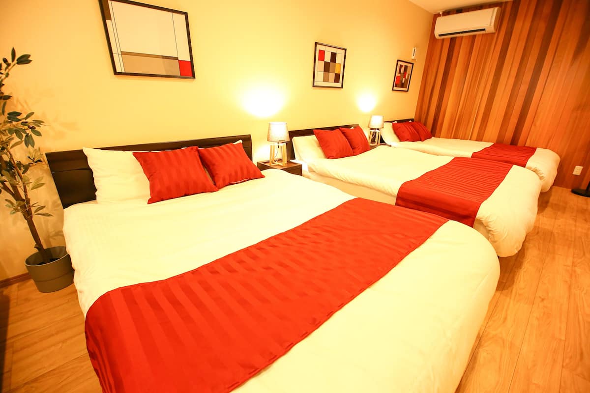 A hotel room with two beds, each with white bedding and red accents, a potted plant, and artwork on the walls.
