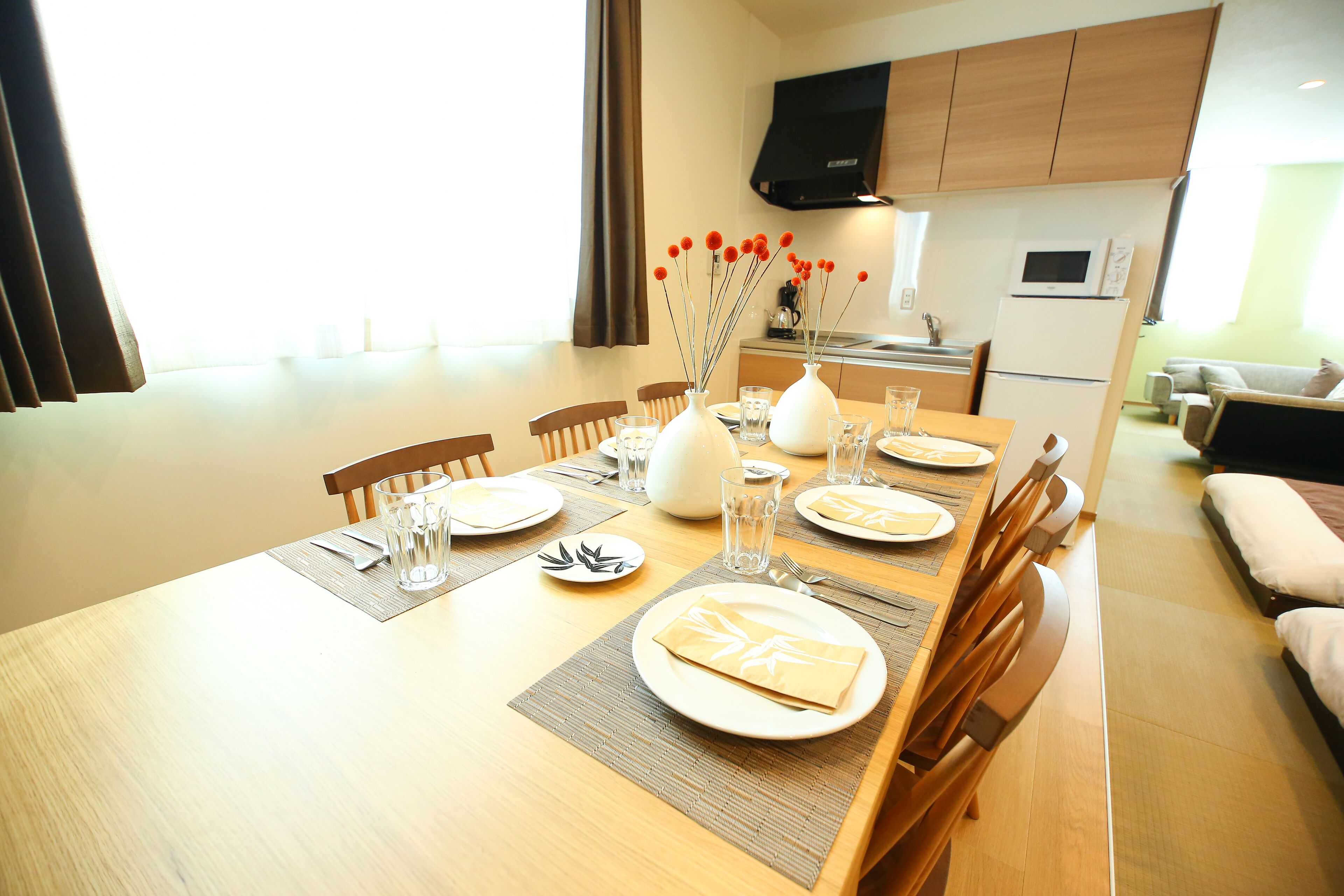 A dining area with a wooden table set for four, including plates, glasses, and a vase with red flowers.