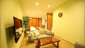 A modern living room with a sofa, coffee table, and a TV. There is a plant and a clock on the wall. - PrimeRoomBeppu Hamawakionsenmae (Beppu)