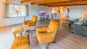 Un soggiorno spazioso con soffitto in legno, televisione e zona pranzo con tavolo e sedie.