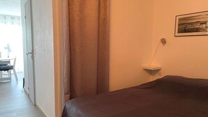 A hotel room with a bed, a small bedside table, a picture on the wall, and a door leading to a balcony.
