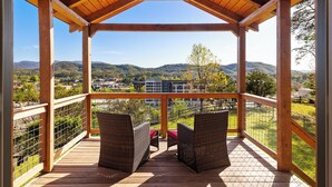 A wooden deck with wicker chairs and a view of a mountainous landscape.