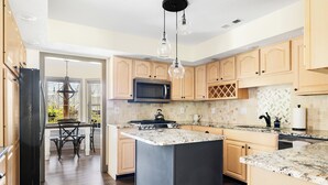 A modern kitchen with wooden cabinets, a granite countertop, a built-in microwave, and a central island.