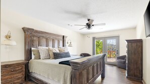 A bedroom with a wooden bed, a ceiling fan, a desk, and a view of the outdoors.
