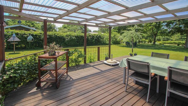 A wooden deck with a table and chairs, surrounded by greenery and a metal railing. - 2 bedroom beautiful home in Samsø (Samsø)