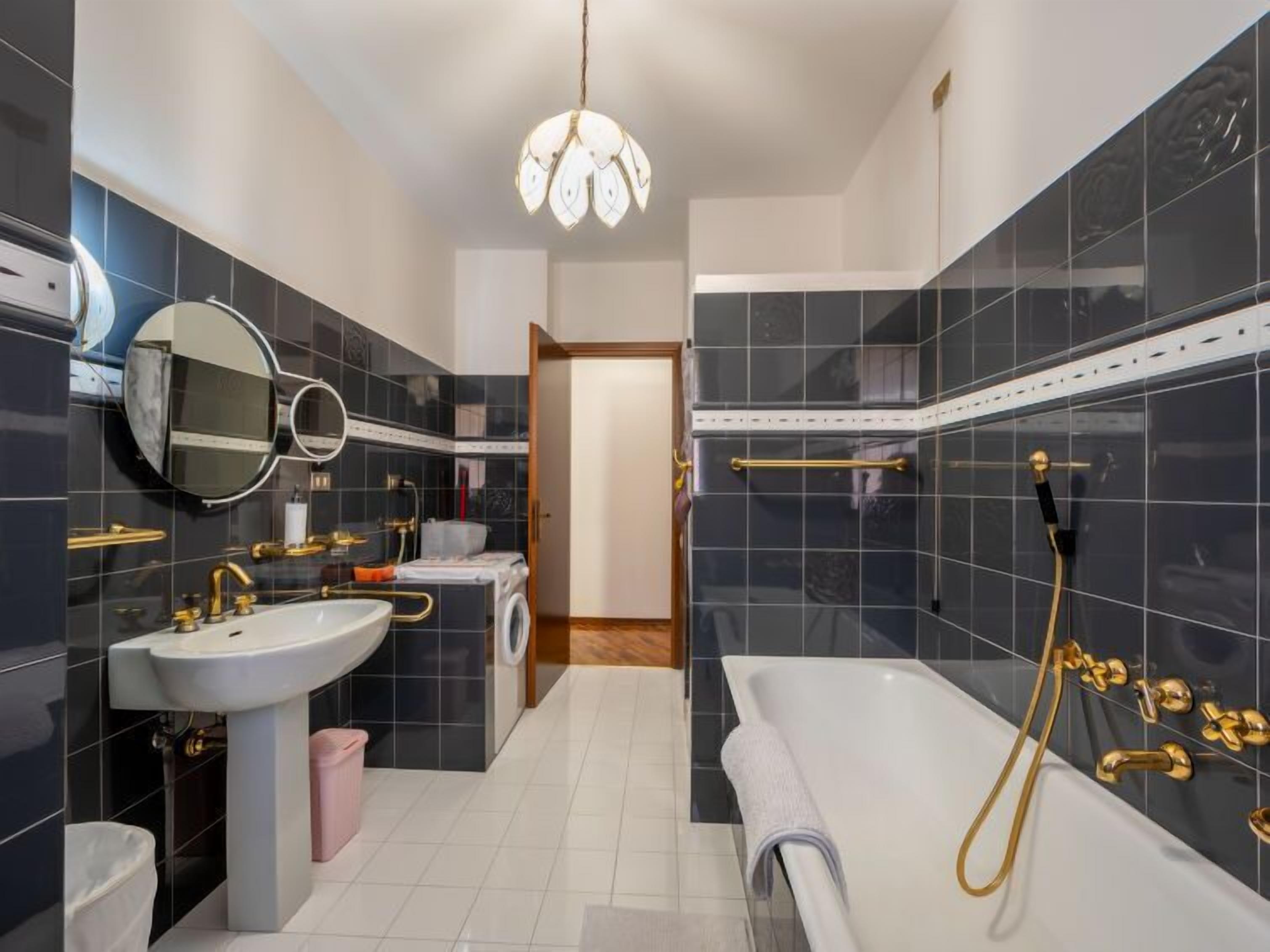 A modern bathroom with a white sink, gold fixtures, a large mirror, and a shower with gold handles.