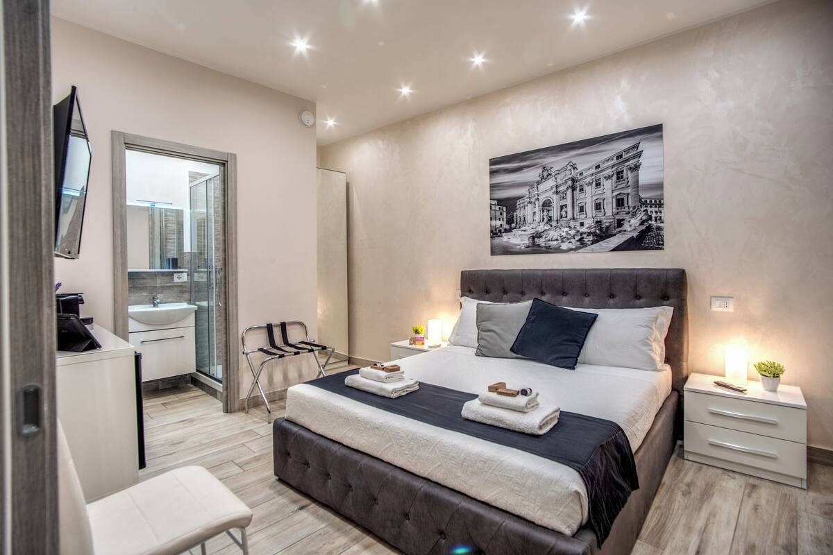 A modern bedroom with a large bed, bedside tables, a desk, and a chair.