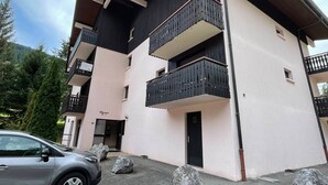 A multi-story building with balconies, a car parked in front, and large rocks in the foreground. - Quiet apartment with parking, near Portes du Soleil (Abondance)