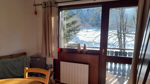 A room with a wooden table, chairs, a radiator, and a window with a view of snow-covered trees. - Quiet apartment with parking, near Portes du Soleil (Abondance)