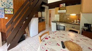 A compact kitchen with wooden cabinets, a refrigerator, a microwave, and a stove. A wooden staircase leads to another level. - Quiet apartment with parking, near Portes du Soleil (Abondance)