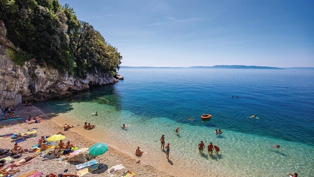 A beach with clear shallow waters, people sunbathing, and a rocky cliff. - Cozy apartment in Rijeka with WiFi (Rijeka)