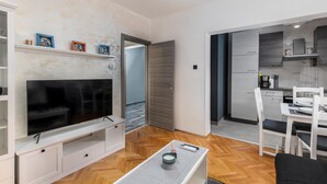 A modern living room with a flat-screen TV, a coffee table, and a dining area with a white table and chairs. - Cozy apartment in Rijeka with WiFi (Rijeka)