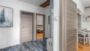 A hallway with a wooden door, a bed in the background, and a dining area with chairs and a table. - Cozy apartment in Rijeka with WiFi (Rijeka)