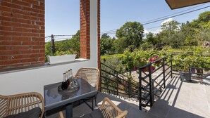 A balcony with a table, chairs, and a view of a garden with various plants and a fence. - Cozy apartment in Rijeka with WiFi (Rijeka)