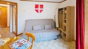 Une pièce comprenant un canapé, une chaise en bois, une table avec un magazine, un porte-manteau et une armoire.
