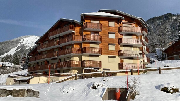 Un hôtel à plusieurs étages, doté de balcons en bois, avec une chaîne de montagnes enneigée en arrière-plan.