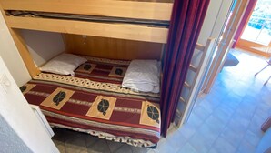 Un lit superposé avec une couvre-lit à motifs, une tête de lit en bois et un rideau rouge.