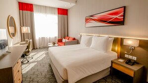 A hotel room with a large bed, a desk with a chair, a TV, and a desk lamp. - Peony Hotel (Dubai)