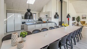 A modern kitchen with a central island, black pendant lights, and a dining area with a long table and chairs. - Stunning home in Samsø with sauna (Samsø)