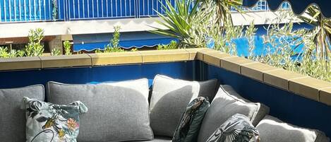 A covered outdoor seating area with a grey sofa, a small round table, and a decorative lantern.