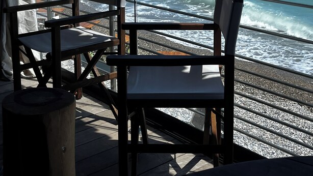 A deck with two chairs and a table, overlooking a rocky shoreline and the ocean.