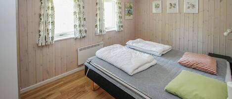Ein Schlafzimmer mit einem Bett, zwei Vorhängen an den Fenstern, einem Heizkörper und einem kleinen Teppich.