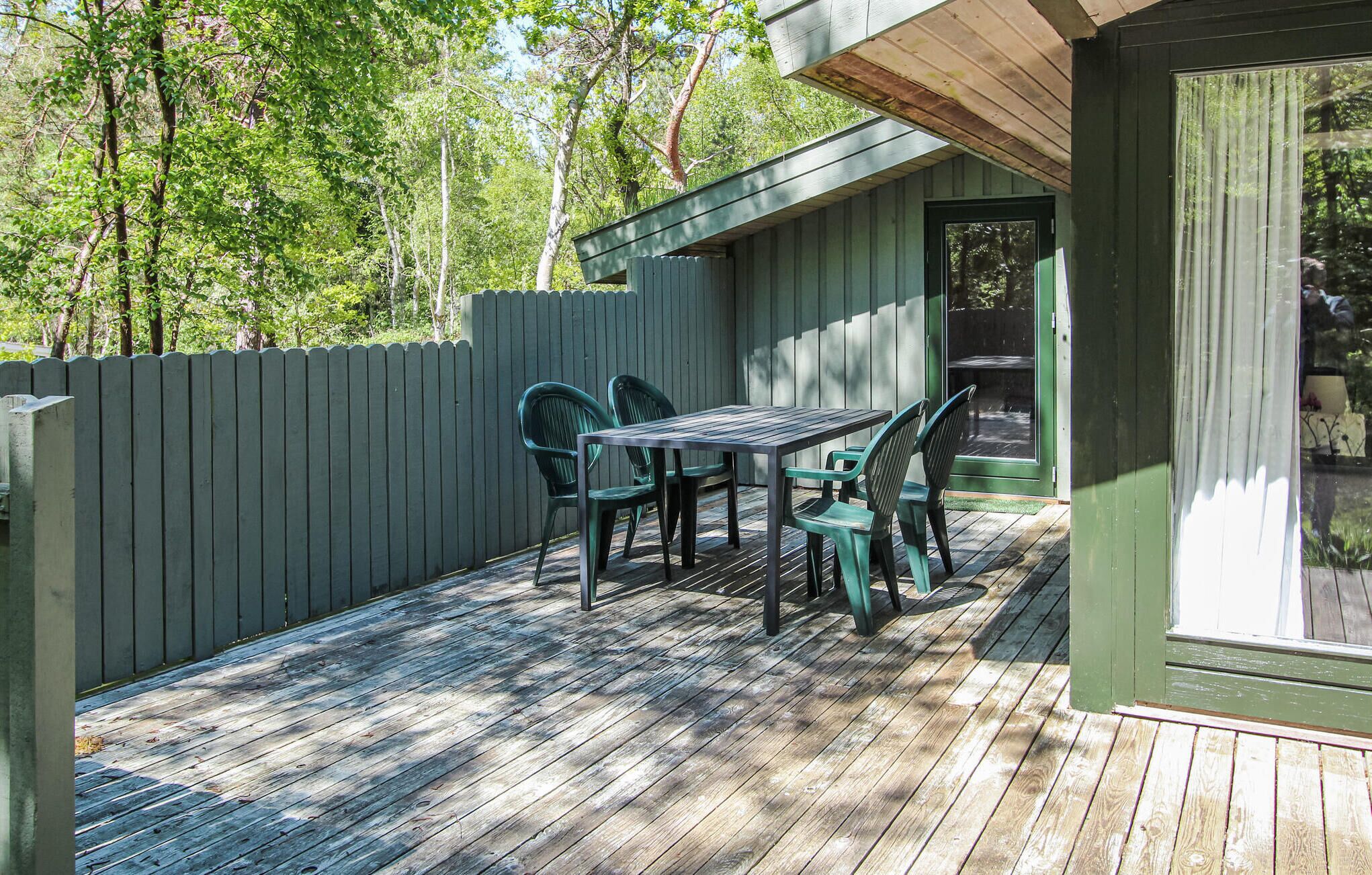 A wooden deck with a table and chairs, a wooden fence, and a building with a door and windows.