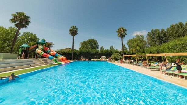Una piscina con tobogán y sillones de descanso a un lado.