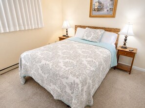 A bedroom with a bed, two bedside tables, a nightstand, a lamp, a window with blinds, and a painting on the wall. - ML176 1st Floor Mountain View Wi-Fi Parking Next to Village and Slopes (Snowshoe)