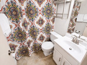 A bathroom with a patterned shower curtain, a toilet, a sink with a mirror, and a towel rack. - ML176 1st Floor Mountain View Wi-Fi Parking Next to Village and Slopes (Snowshoe)