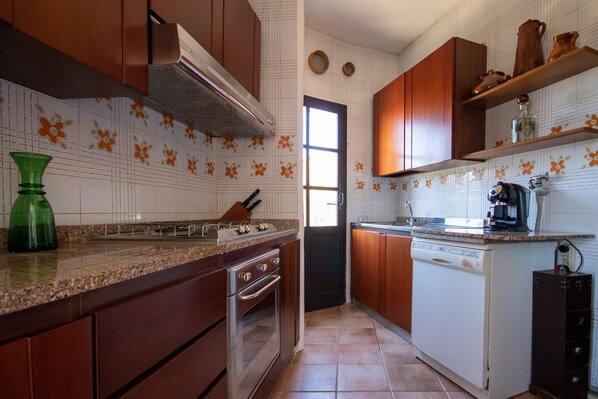 A kitchen with wooden cabinets, a built-in oven, a dishwasher, and a countertop with a green glass vase. - Villa with a pool and a view of the sea (Torre Delle Stelle (Maracalagonis))
